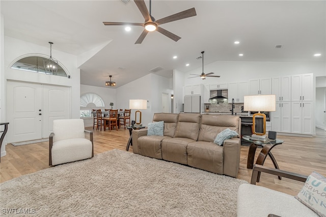 living room with vaulted ceiling, sink, ceiling fan with notable chandelier, and light wood-type flooring