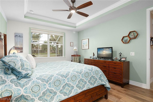 bedroom featuring ceiling fan, a raised ceiling, light wood-type flooring, and crown molding