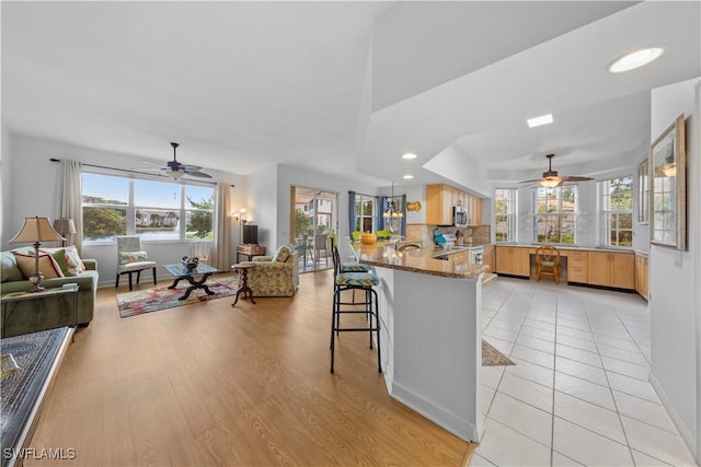 kitchen with light wood-type flooring, kitchen peninsula, a breakfast bar area, decorative backsplash, and light stone countertops