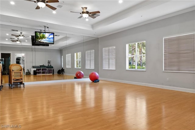 workout area featuring a tray ceiling, ornamental molding, light hardwood / wood-style floors, and ceiling fan