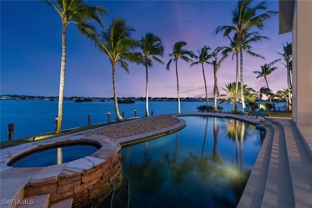 pool at dusk featuring a water view and an in ground hot tub