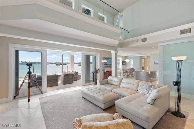 living room with light tile patterned floors, decorative columns, a high ceiling, and a water view