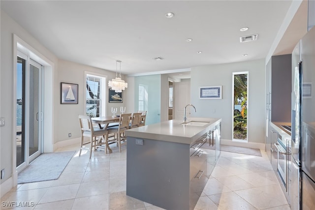 kitchen featuring pendant lighting, a kitchen bar, a center island with sink, sink, and a chandelier