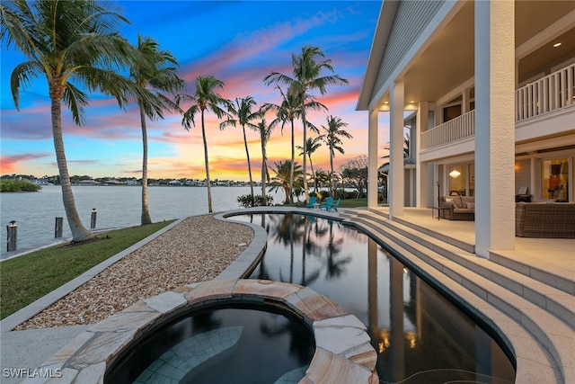 pool at dusk featuring an in ground hot tub, a water view, and a patio area