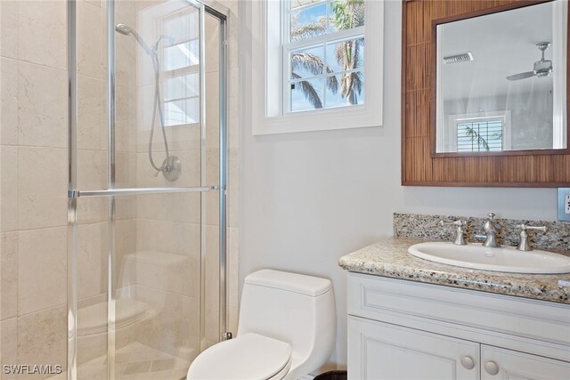 bathroom with vanity, a shower with shower door, toilet, and a healthy amount of sunlight