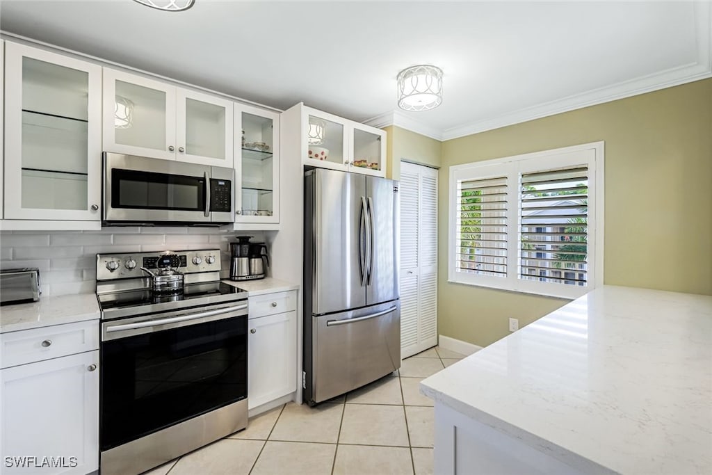 kitchen with stainless steel appliances, ornamental molding, tasteful backsplash, and white cabinetry