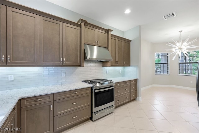 kitchen with a chandelier, light tile patterned flooring, stainless steel gas range oven, backsplash, and light stone countertops