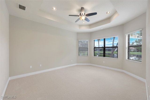 unfurnished room featuring a tray ceiling, light carpet, and ceiling fan