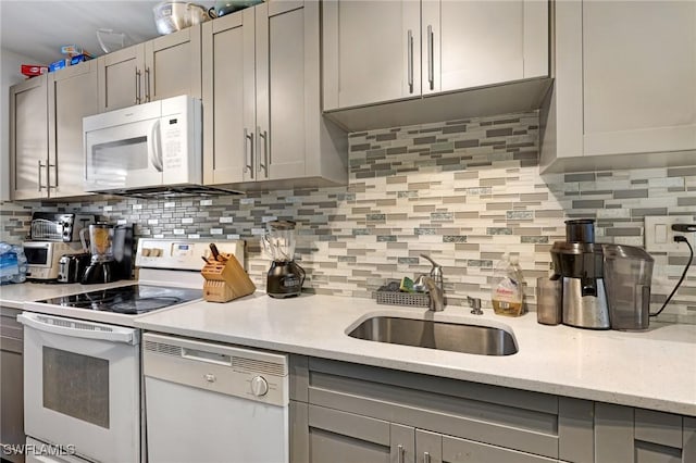 kitchen with gray cabinetry, sink, light stone counters, backsplash, and white appliances