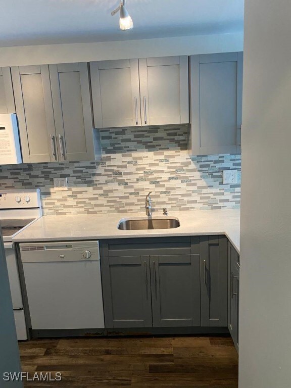 kitchen with stove, backsplash, white dishwasher, sink, and gray cabinets