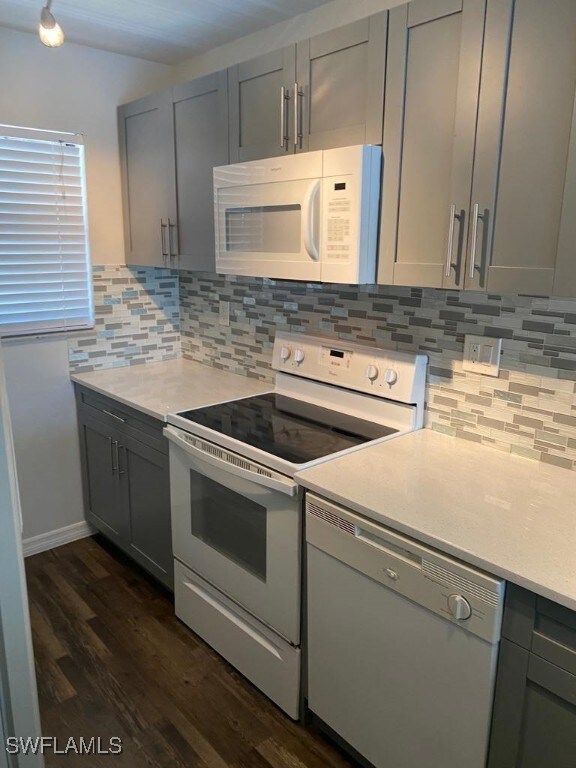 kitchen featuring decorative backsplash, dark hardwood / wood-style flooring, white appliances, and gray cabinetry