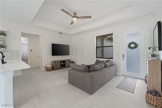 living room with ceiling fan, a tray ceiling, and crown molding