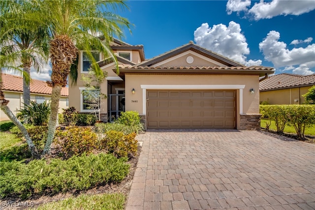 view of front of home featuring decorative driveway, stone siding, an attached garage, and stucco siding