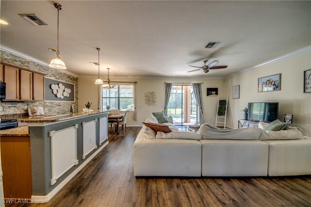 living area featuring dark wood-style flooring, visible vents, crown molding, and ceiling fan with notable chandelier