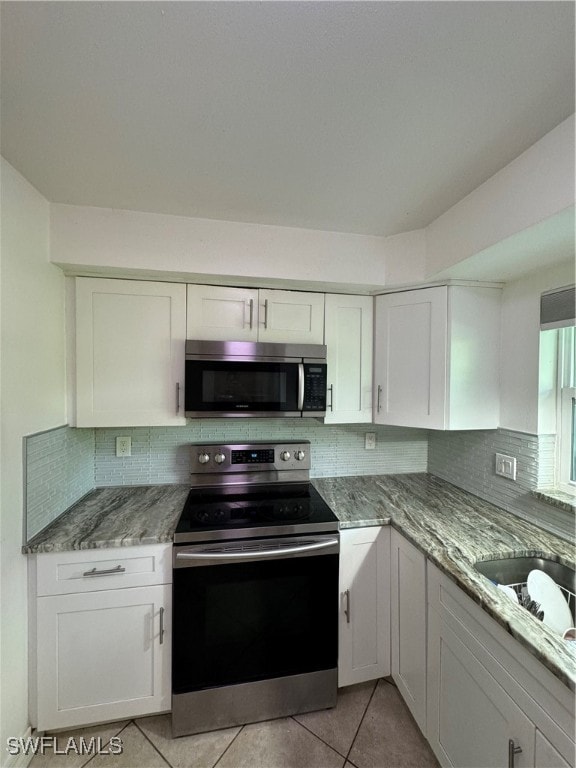 kitchen with stainless steel appliances, decorative backsplash, light tile patterned floors, and white cabinets