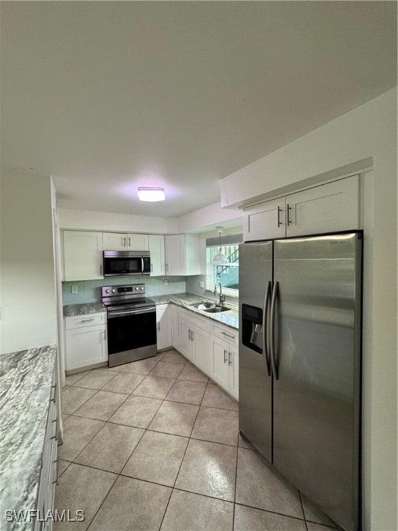 kitchen with appliances with stainless steel finishes, white cabinetry, sink, and light tile patterned floors