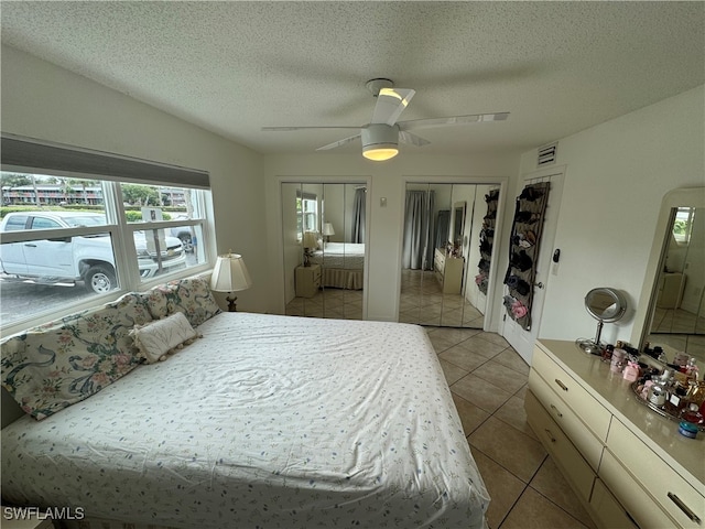 tiled bedroom featuring ceiling fan, multiple closets, and a textured ceiling