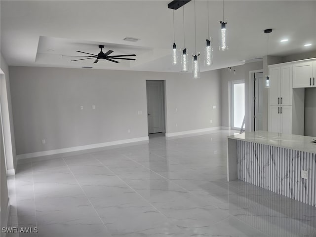 kitchen featuring pendant lighting, ceiling fan, a raised ceiling, white cabinetry, and light stone counters