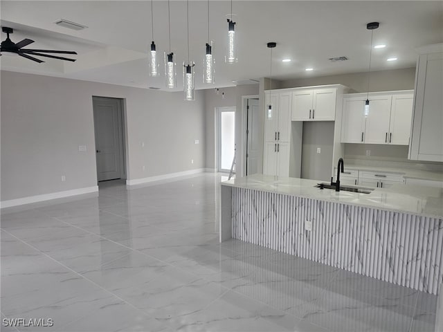 kitchen featuring decorative light fixtures, white cabinetry, ceiling fan, sink, and light stone counters