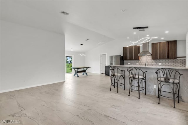 kitchen featuring wall chimney exhaust hood, kitchen peninsula, stainless steel fridge, lofted ceiling, and a breakfast bar area