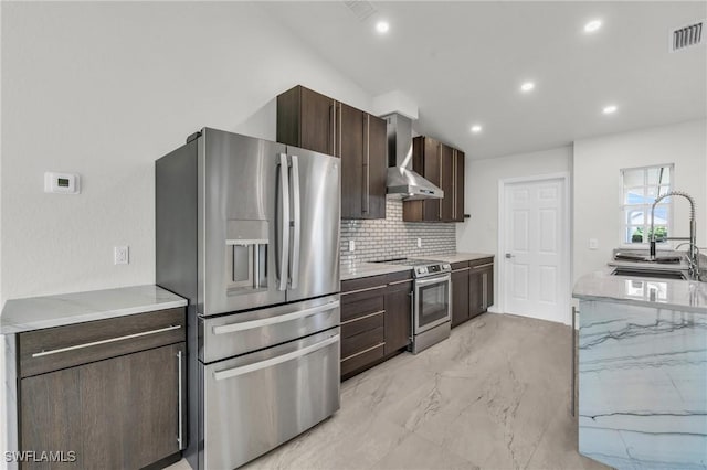 kitchen featuring light stone countertops, appliances with stainless steel finishes, tasteful backsplash, wall chimney exhaust hood, and sink