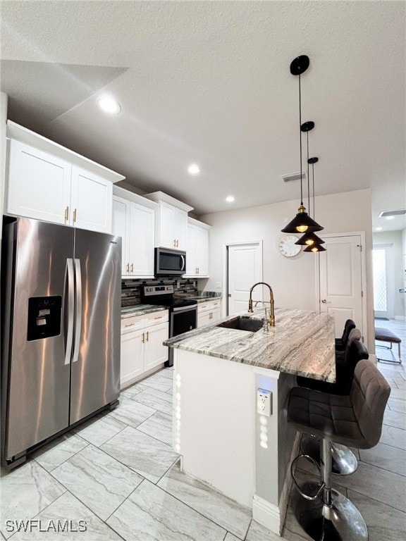 kitchen featuring white cabinets, appliances with stainless steel finishes, light stone countertops, sink, and decorative light fixtures