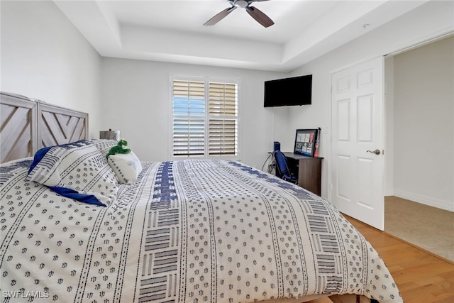 bedroom featuring wood-type flooring, a tray ceiling, and ceiling fan