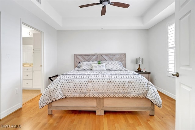 bedroom featuring wood-type flooring, connected bathroom, a tray ceiling, and ceiling fan