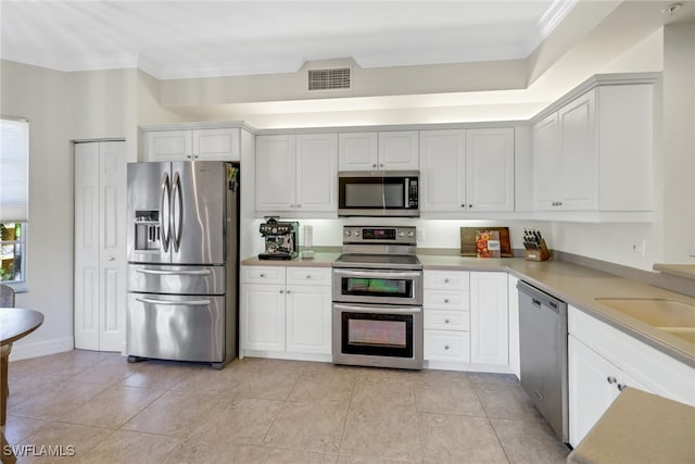 kitchen with appliances with stainless steel finishes, crown molding, light tile patterned floors, and white cabinets