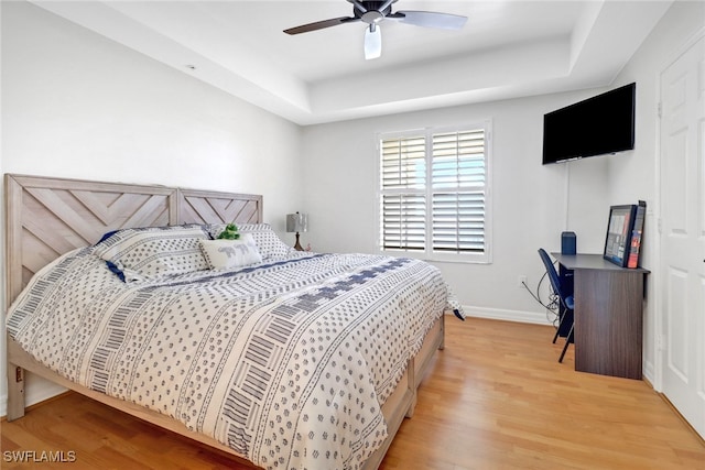 bedroom featuring ceiling fan, a raised ceiling, and light hardwood / wood-style floors