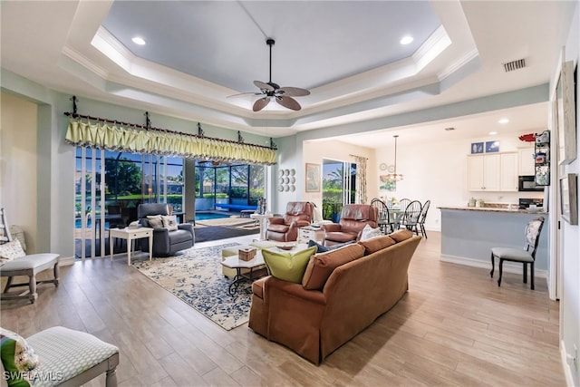 living room with ceiling fan, a raised ceiling, and light wood-type flooring