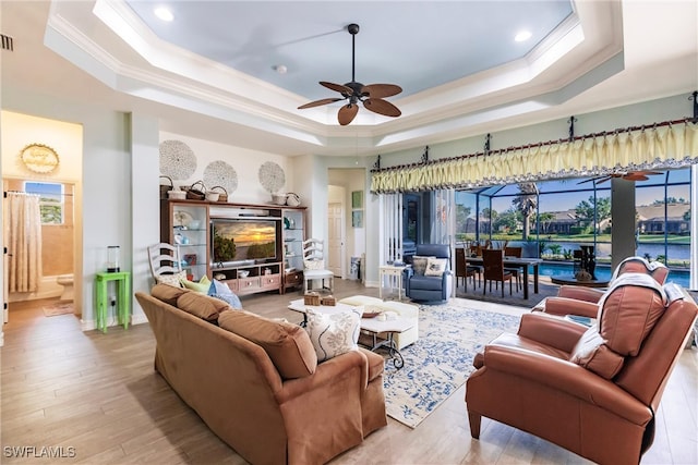 living room featuring a raised ceiling, ceiling fan, and light hardwood / wood-style flooring