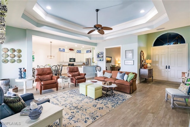 living room featuring ceiling fan, a raised ceiling, light wood-type flooring, and crown molding