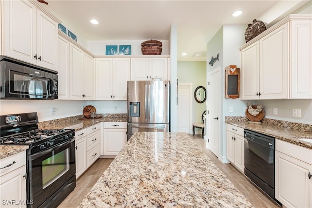 kitchen with black appliances, white cabinetry, light stone countertops, and light hardwood / wood-style flooring