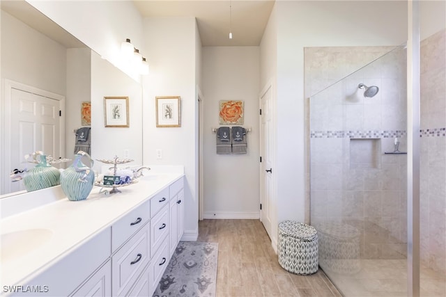 bathroom with wood-type flooring, vanity, and a tile shower