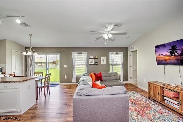 living room featuring dark wood-type flooring, ceiling fan with notable chandelier, a healthy amount of sunlight, and lofted ceiling