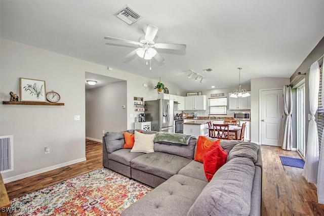 living room featuring lofted ceiling, rail lighting, ceiling fan with notable chandelier, and hardwood / wood-style flooring