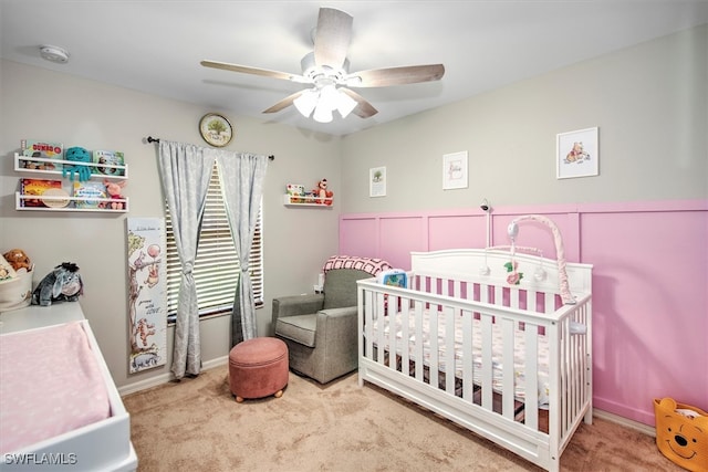 carpeted bedroom featuring ceiling fan and a nursery area