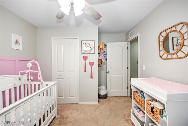 bedroom featuring light carpet, a nursery area, a closet, and ceiling fan