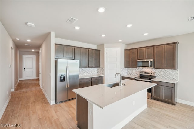 kitchen featuring light stone counters, an island with sink, sink, appliances with stainless steel finishes, and light wood-type flooring