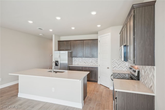 kitchen featuring an island with sink, stainless steel appliances, light wood-type flooring, and sink