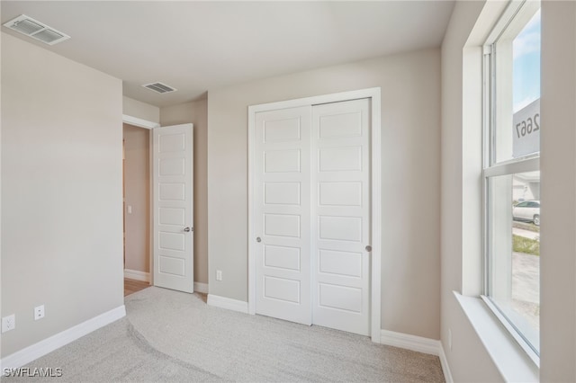 unfurnished bedroom with multiple windows, light colored carpet, and a closet