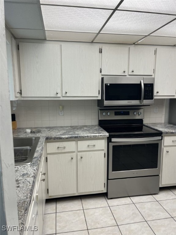 kitchen featuring stainless steel appliances, a paneled ceiling, light tile patterned flooring, and tasteful backsplash