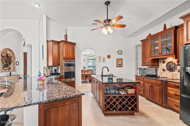 kitchen featuring glass insert cabinets, arched walkways, brown cabinetry, and a center island with sink