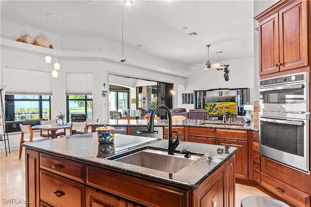 kitchen featuring an island with sink, dark stone counters, open floor plan, and a sink