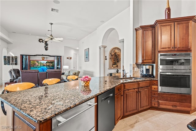 kitchen featuring dishwashing machine, stainless steel double oven, a sink, open floor plan, and dark stone counters