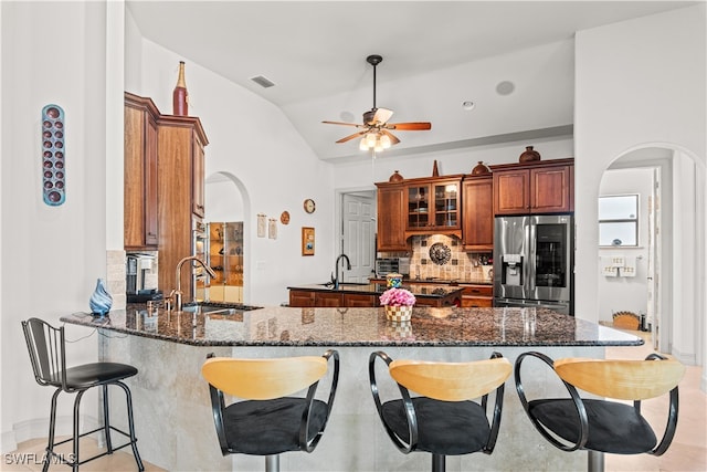 kitchen featuring arched walkways, refrigerator with glass door, dark stone counters, and a sink