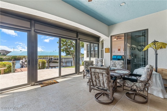 dining area with a sunroom, a water view, a textured wall, and a textured ceiling