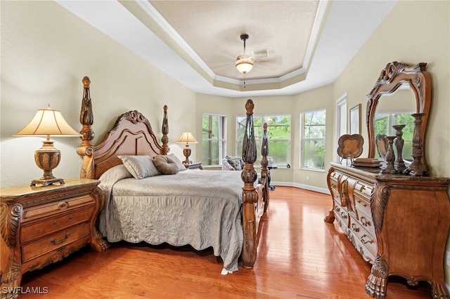 bedroom with wood-type flooring, ornamental molding, and a raised ceiling