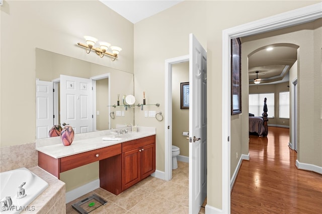 bathroom featuring tiled tub, vanity, hardwood / wood-style flooring, toilet, and ceiling fan